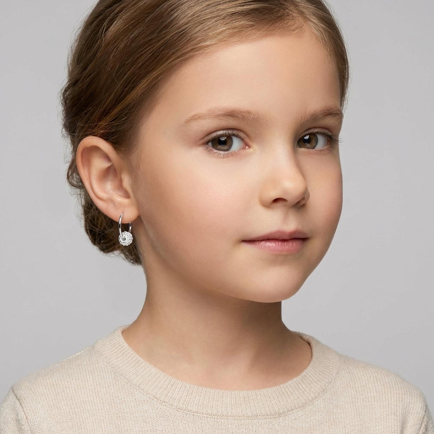 Young girl wearing silver kids crystal ball charm earrings with sparkling clear crystals by Melchior Jewellery