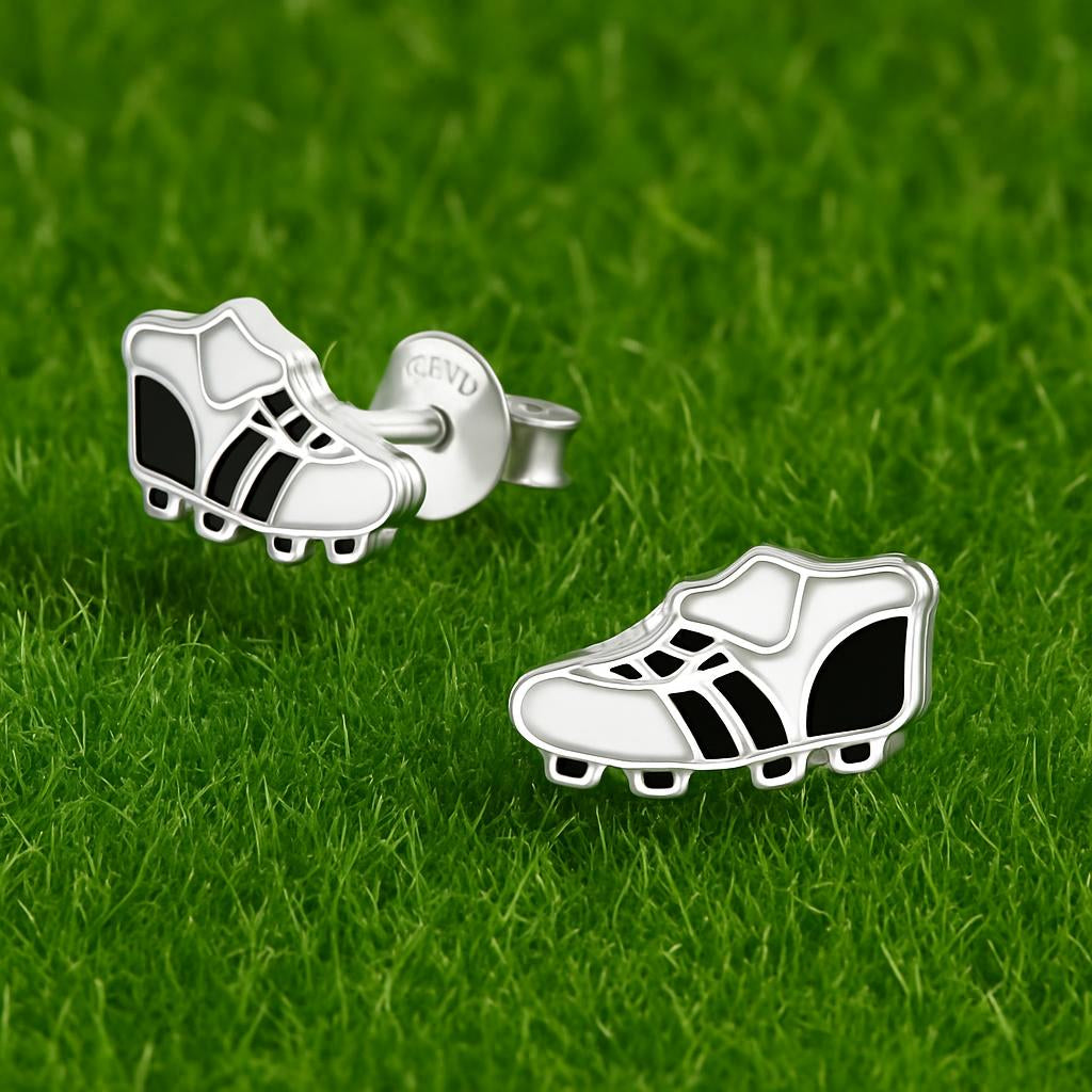 Melchior Jewellery kids football boot stud earrings in silver and black on green grass background