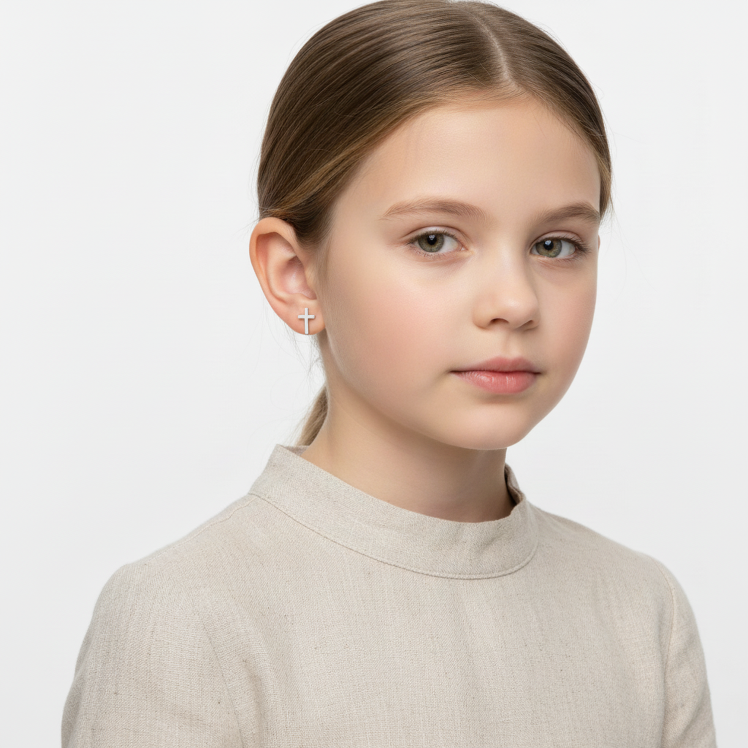 Young girl wearing kids silver cross stud earrings from Melchior Jewellery with simple beige top
