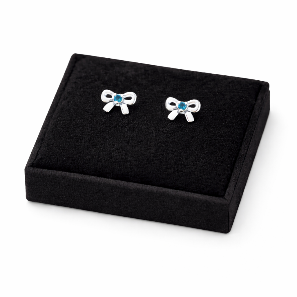 Melchior Jewellery March birthstone earrings for kids shaped as silver bows with blue stones on black display