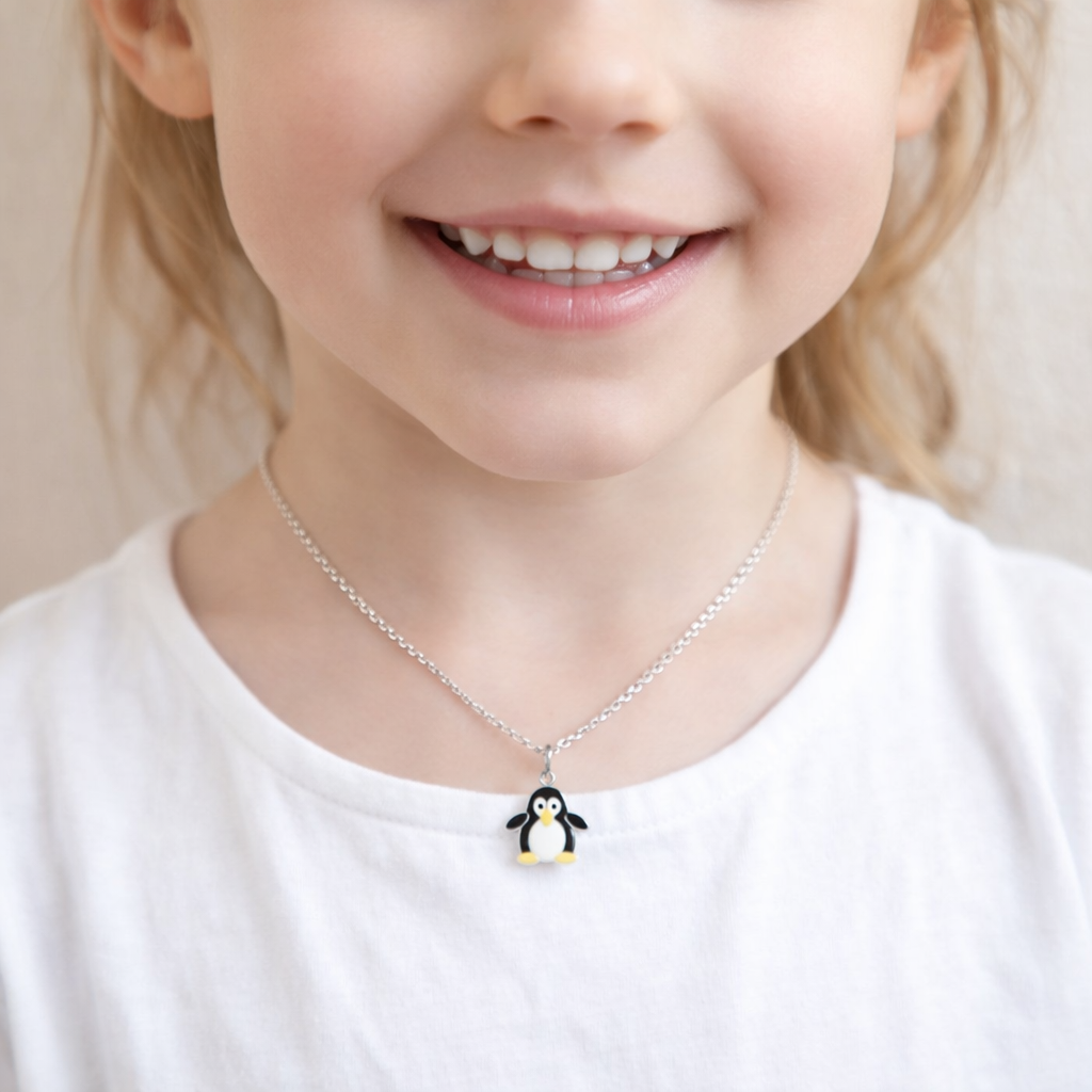 Silver chain penguin necklace with black and white enamel pendant worn by child in white top