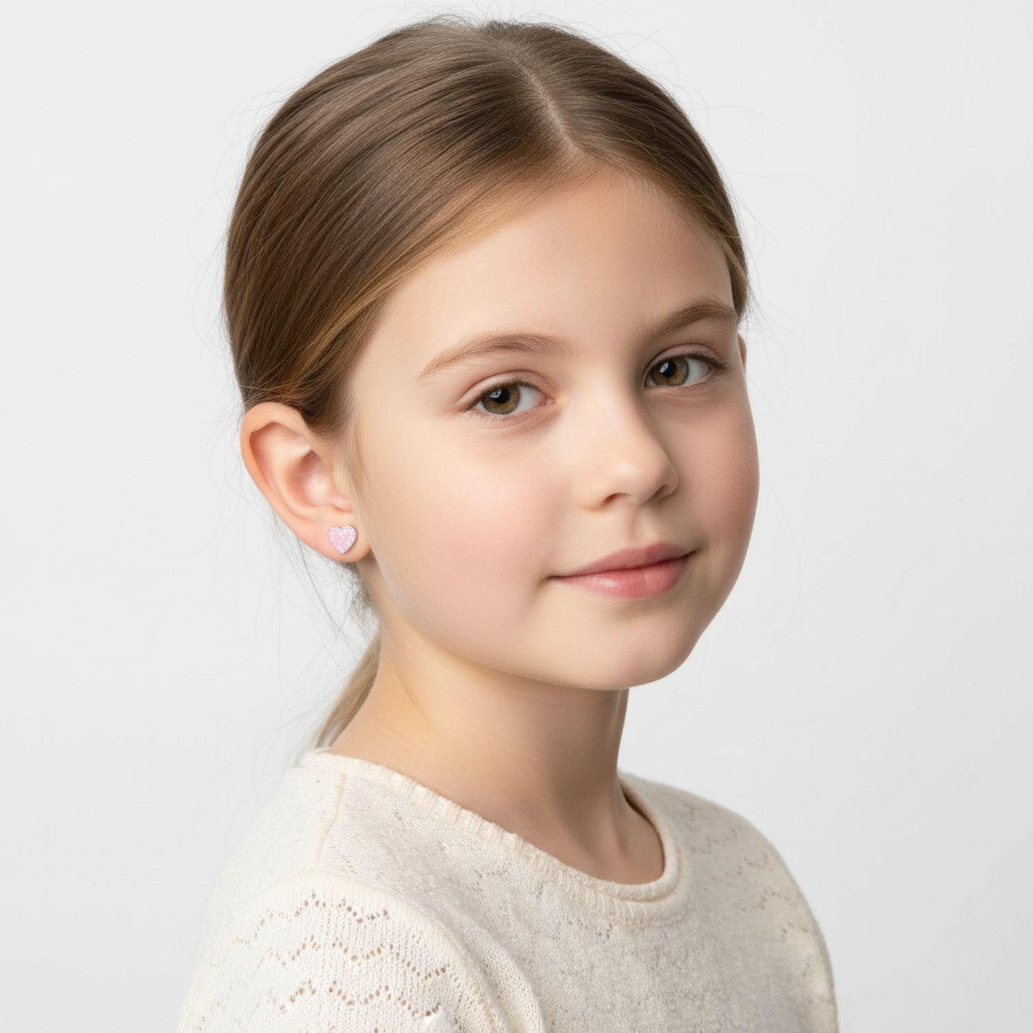 Young girl wearing pink glitter heart stud earrings for kids by Melchior Jewellery in a close-up portrait