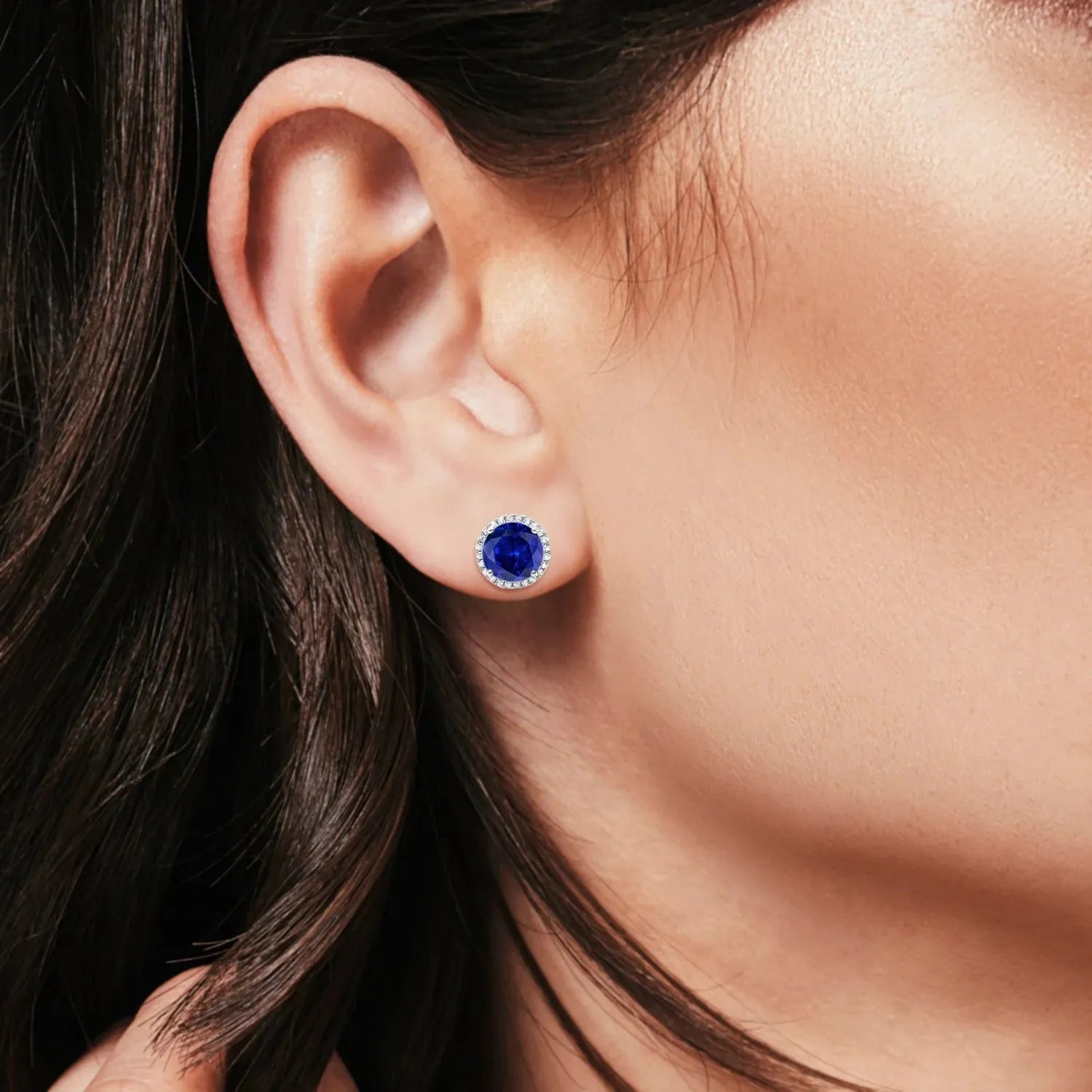 Close-up of sapphire wedding stud earrings silver with deep blue sapphire centre and silver halo worn on ear
