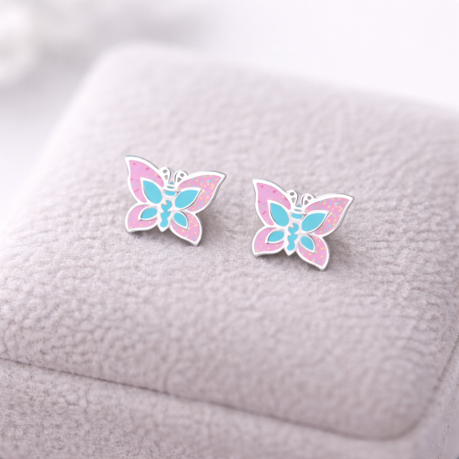 Melchior Jewellery sparkly butterfly stud earrings for kids in pink and blue on soft display