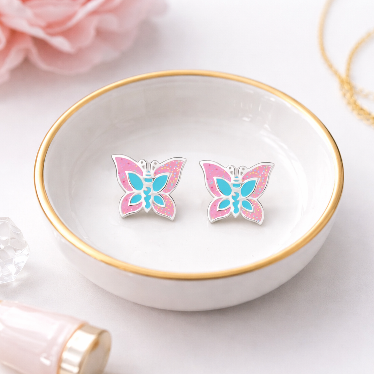 Melchior Jewellery sparkly butterfly stud earrings for kids in pink and blue displayed in a white dish