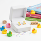 Sparkly duck stud earrings for kids displayed in a white box surrounded by colourful rubber ducks and children's books