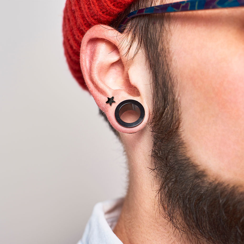 Close up of ear with black tunnel plug and sterling silver star cartilage earring by Melchior Jewellery