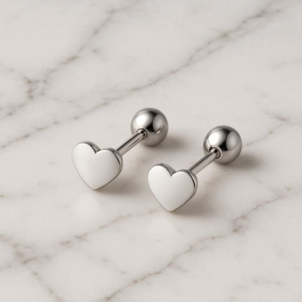 Melchior Jewellery titanium heart stud earrings in silver-tone on marble surface