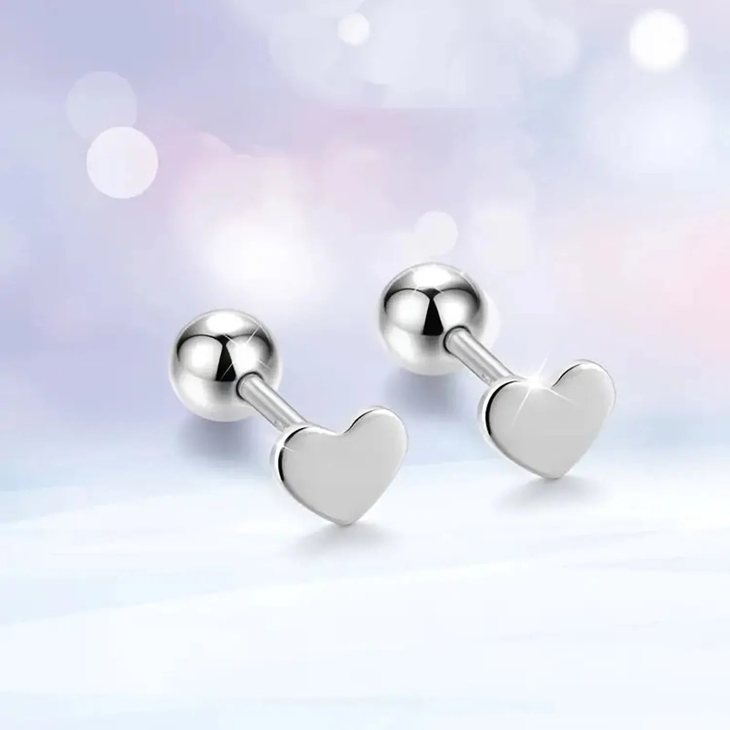titanium heart stud earrings in polished silver finish on soft pastel background