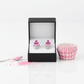 Pink cupcake earrings for children displayed in a black box with pink baking cups and sprinkles