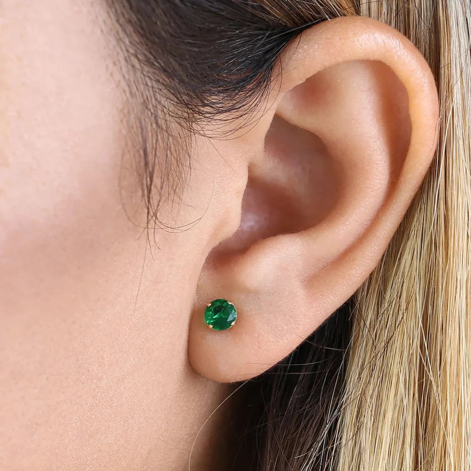 14K yellow gold emerald earrings featuring vibrant green round emerald studs on a pierced ear