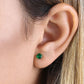 14K yellow gold emerald earrings worn on ear close-up showing vibrant green gemstone stud