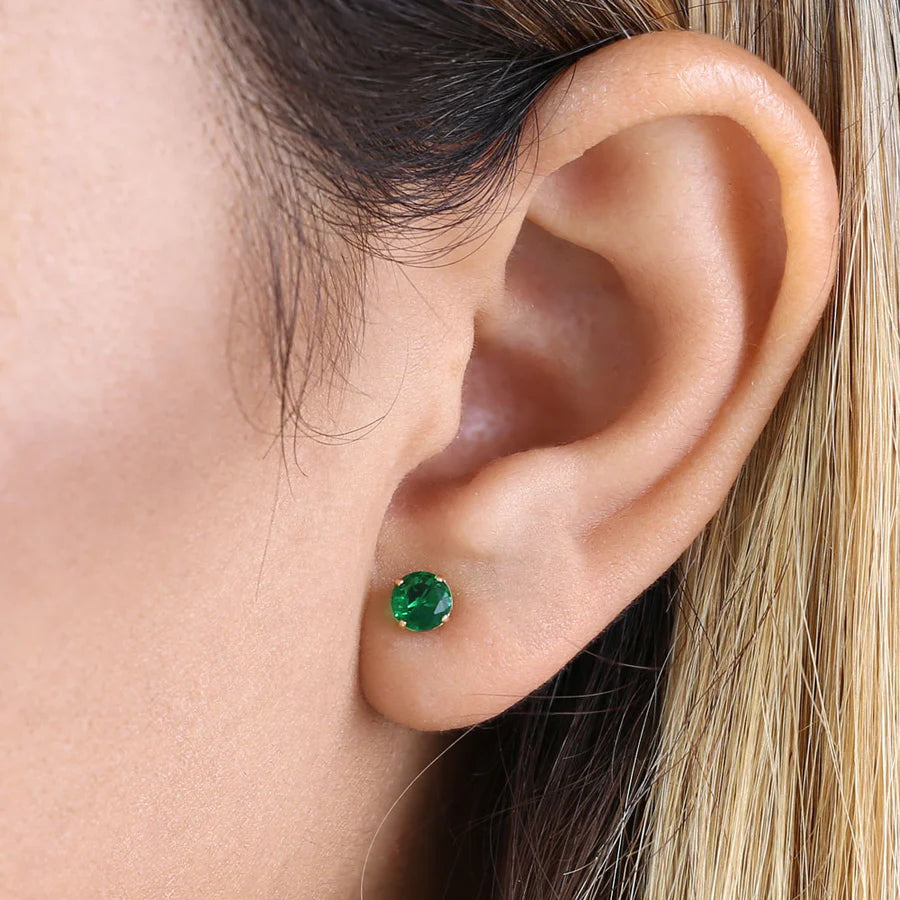 14K yellow gold emerald earrings worn on ear close-up showing vibrant green gemstone stud