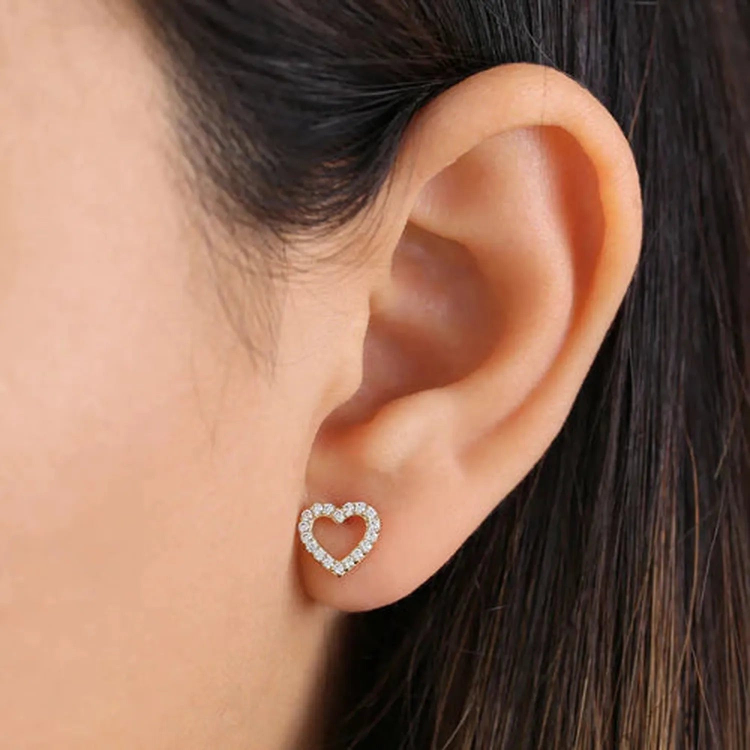 Delicate 14k yellow gold heart earrings with diamonds worn on ear by Melchior Jewellery