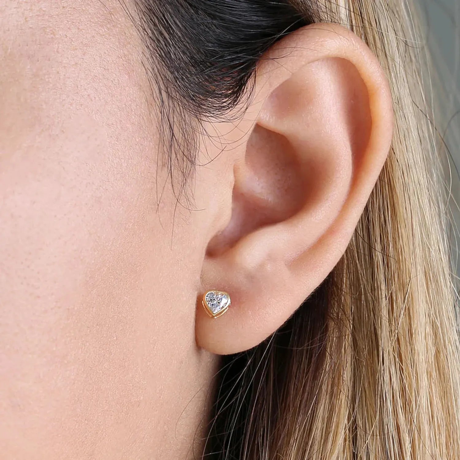 14K yellow gold heart stud earrings with clear sparkling stones worn on ear by Melchior Jewellery
